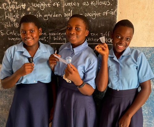 Three schoolgirls smiling with their menstrual cups