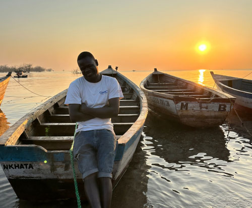 Man stood by a fishing boat at sunset